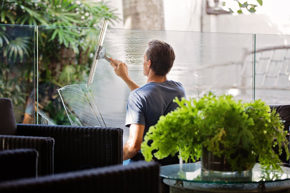 Professional window cleaner using squeegee to treat severe hard water stains on large glass surface