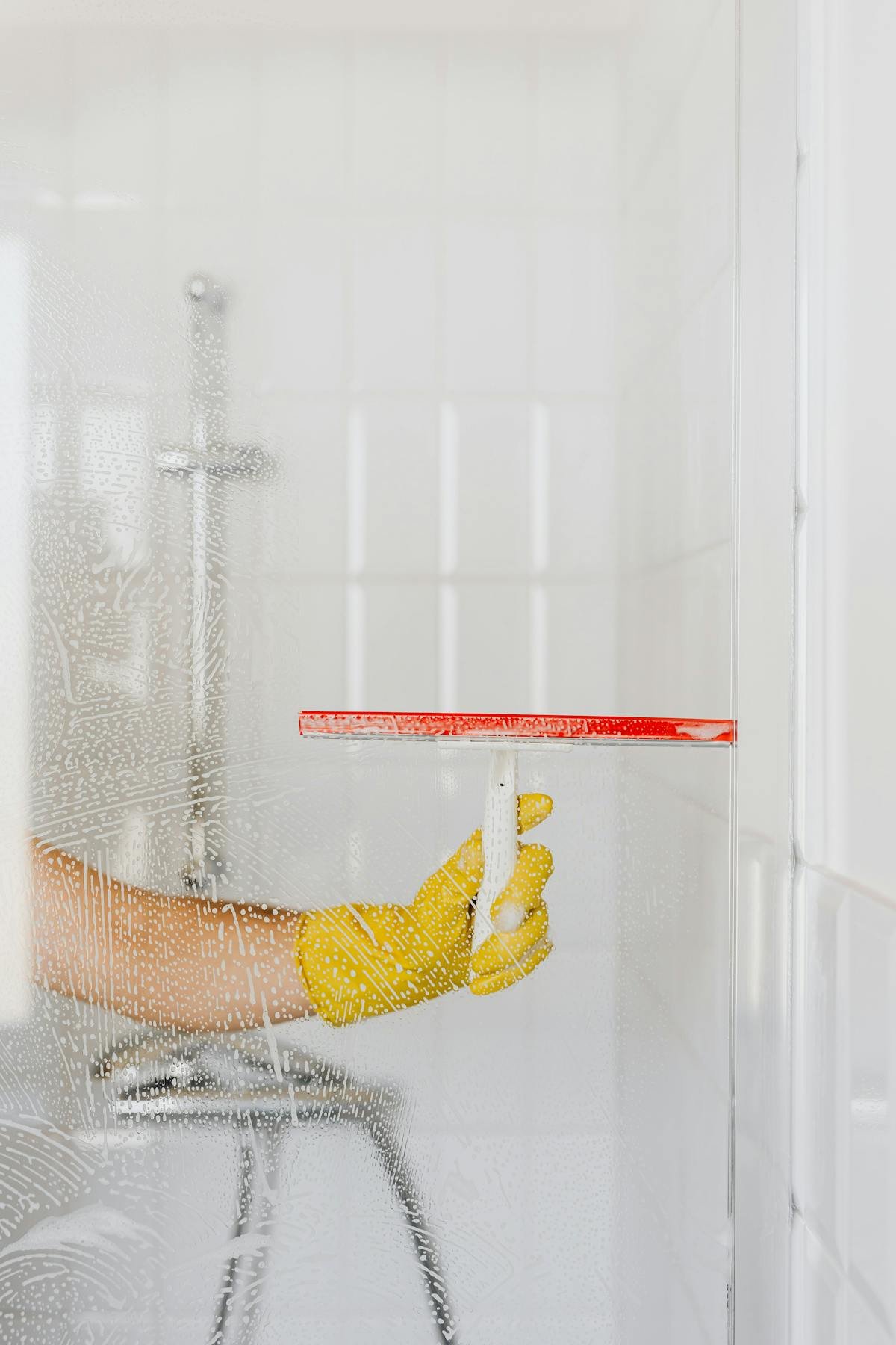 Gloved hand using squeegee to clean glass with hard water stains