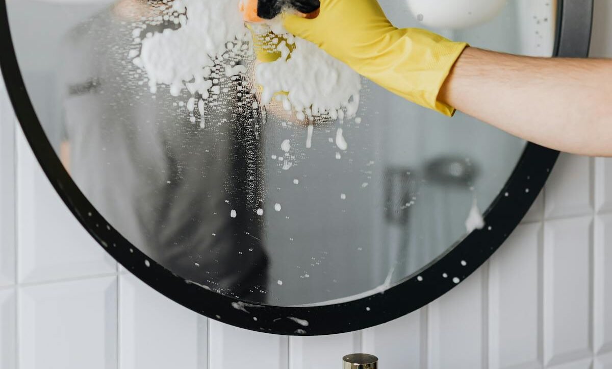 Yellow-gloved hand using squeegee on soapy glass for streak-free windows
