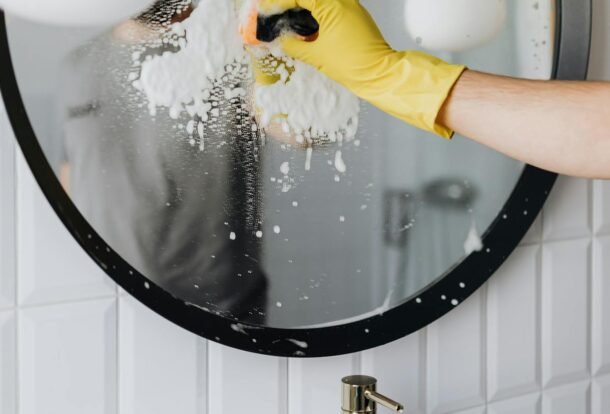 Yellow-gloved hand using squeegee on soapy glass for streak-free windows