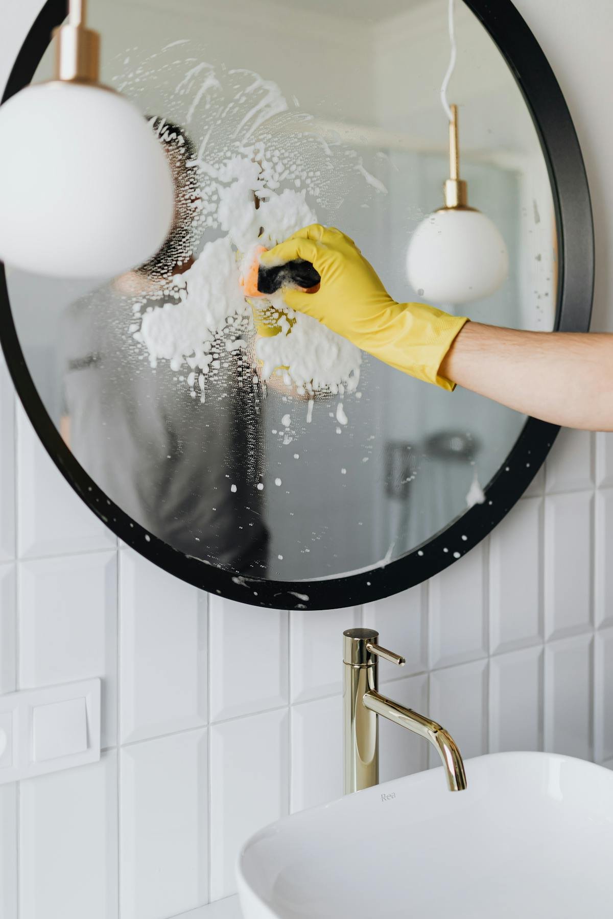 Yellow-gloved hand using squeegee on soapy glass for streak-free windows