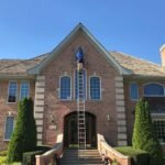 Professional window washer on a ladder cleaning a brick home — the benefits of clean windows start outside