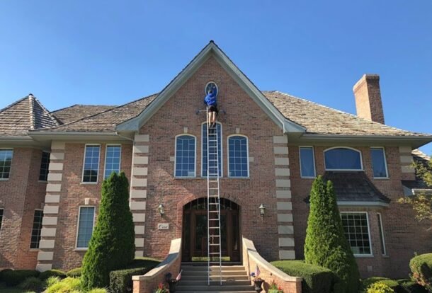 Professional window washer on a ladder cleaning a brick home — the benefits of clean windows start outside