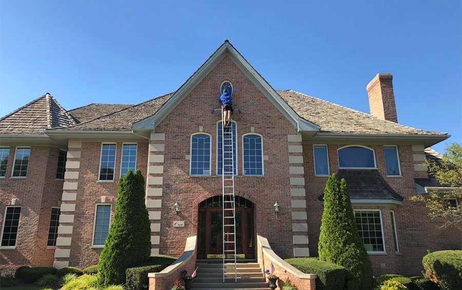 Professional window washer on a ladder cleaning a brick home — the benefits of clean windows start outside