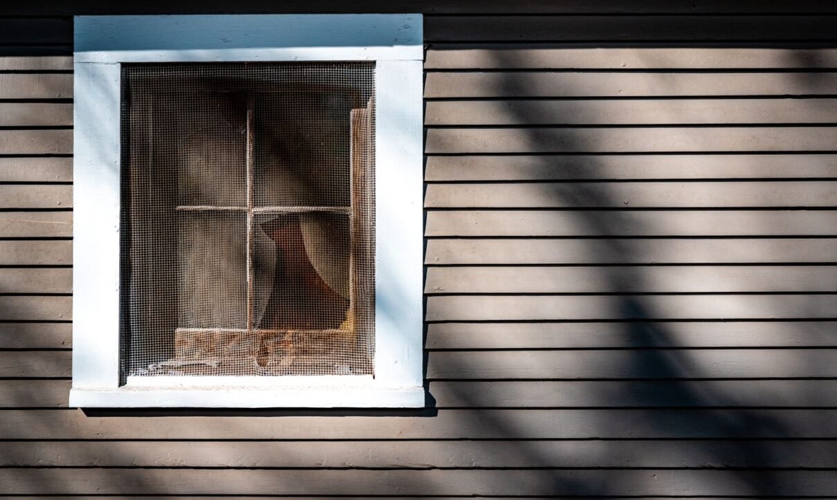 House window covered by an insect screen in afternoon sun